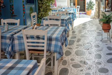 Fototapeta na wymiar Outdoors tavern restaurant Greece, Tinos island Hora town Cyclades. Empty chair table, summer day.