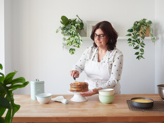 woman in white apron decorating chocolate cake with caramel cream at home