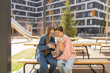 Happy teen friends using smartphone in park