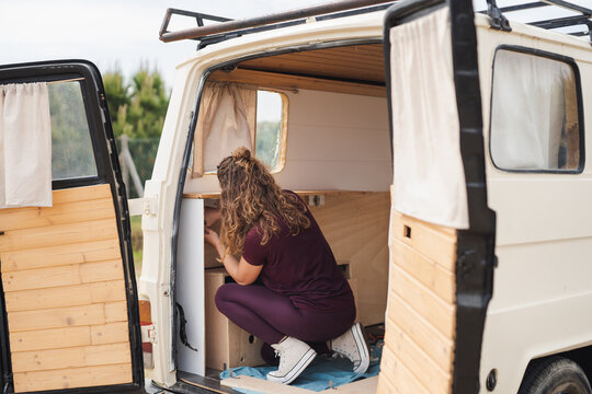Anonymous woman repairing wooden cupboard in van with open door