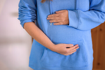 Młoda kobieta trzyma się za ciążowy brzuch.
