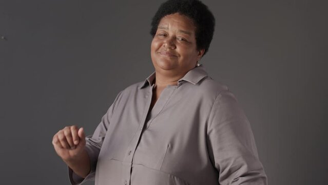 Medium portrait of happy adult plus size Black woman dancing energetically at camera standing on grey background
