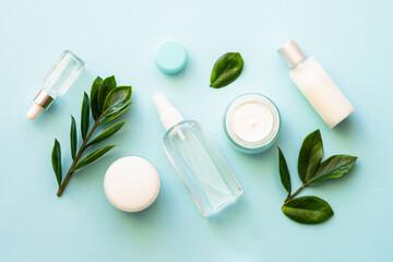 Natural cosmetic products. Cream, serum, tonic with green leaves. Flat lay on blue background.