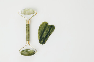 Facial jade massage rollers and gua sha massagers made from green quartz stone on white background