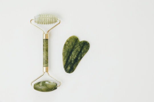 Facial jade massage rollers and gua sha massagers made from green quartz stone on white background