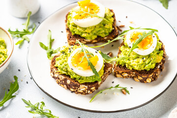Open sandwich. Whole grain bread with avocado and boiled eggs. Top view on white kitchen table.