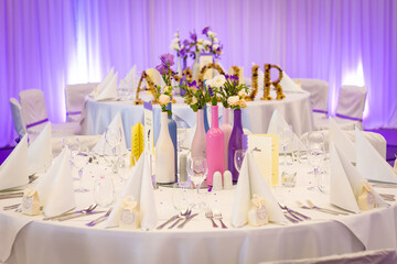 wedding table decoration / setting. a round table with white linens and purple lighting. AMOUR sign in the background