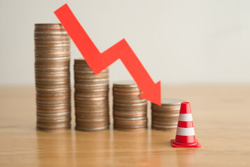 Traffic warning cone and stack coins with red chart trending downturn background on wooden table. FED fix great economy recession crisis, inflation, stagflation, bank run, business and financial loss
