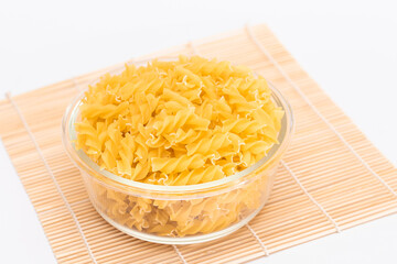 Uncooked Chifferi Rigati Pasta in Glass Jar on Bamboo Mat on White Background. Fat and Unhealthy Food. Classic Dry Macaroni. Italian Culture and Cuisine. Raw Pasta