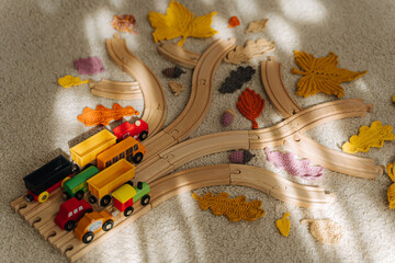 Tree made from toy wooden railway with toy train and autumn leaves on the floor in children room. Fall activity for kids.