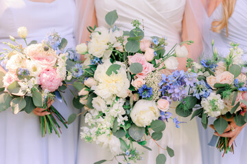 A bride and her bridesmaids stand next to each other and hold wildflower flowers bouquet in shades of ivory, pink, and purple