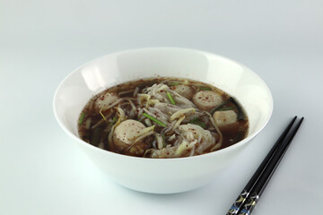 thai local blood noodle with meat balls called boat noodle is famous street food served on the white table with black chopsticks during lunch in the local noodle shop in Thailand
