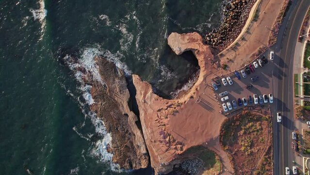 Beautiful sunset cliffs public nature park near San Diego in southern California during sunset golden hour from an above drone and aerial view moving over rocks, Pacific Ocean waves, and car traffic
