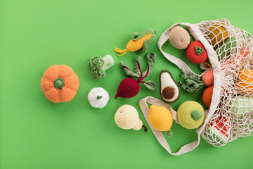 Cute knitting vegetables and fruits for activity, motor and sensory development. Eco friendly toys in cotton bag on green table. - obrazy, fototapety, plakaty