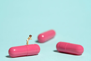 Miniature tiny people toy figure photography. A toddler baby walking above pink medicine pill tablet capsule. Isolated on blue background