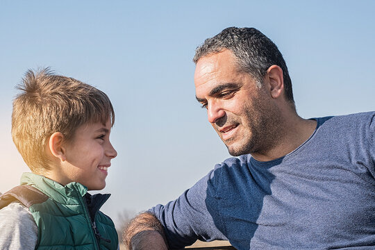 Father Gesturing And Talking With Teenager Son In Park