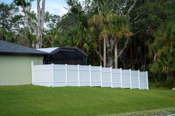 Fototapeta na wymiar White vinyl picket fence on green lawn surrounding property grounds for backyard protection and privacy