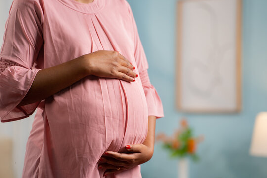 Close up shot of Pregnant woman standing by touching or feeling tummy at home - concept of expecting baby, motherhood and Emotional connection.