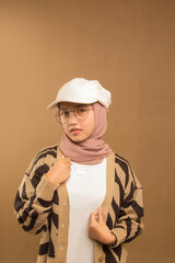portrait of beautiful young woman in glasses and hat in white negligee and brown sweater standing with piercing eyes, on white studio background