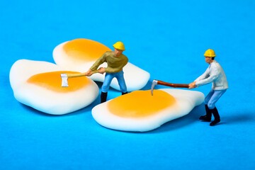 Conceptual image of miniature figure people trying to burst the yolks of fried egg candy sweets