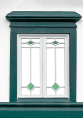 Janela com caixilhos de madeira brancos, ombreiras verdes e vidros transparentes. 
