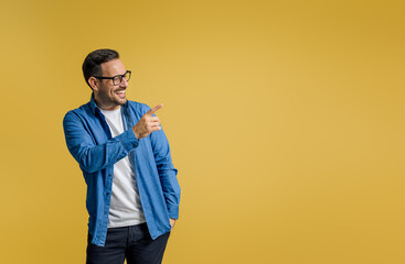 Happy businessman pointing away at copy space for advertisement while standing on yellow background