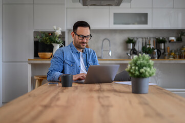 Focused male entrepreneur working over laptop on wooden desk in home office, with glasses