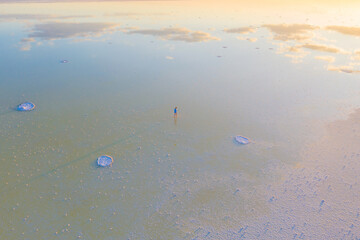 A girl in a blue dress walks along the shore of a salt lake with mirrored sky and clouds at sunset