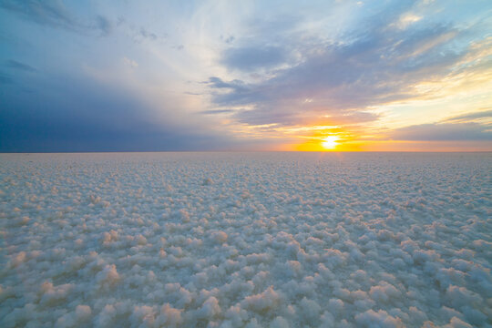 A girl in a blue dress walks along the shore of a salt lake with mirrored sky and clouds at sunset