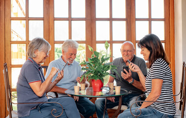 Happy Group of Senior Caucasian People Sitting at Restaurant Table Enjoying Coffee Cup and Using Phone