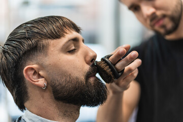 Barber combing and grooming his client's mustache with a small round brush in the barber shop.