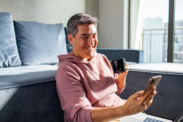 MIddle aged latin man using a smart phone on a couch at home