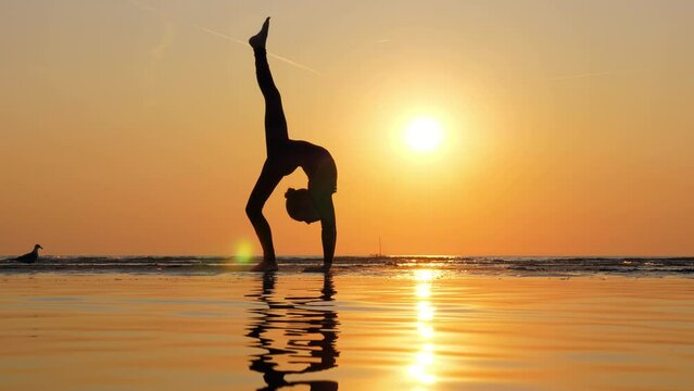 In mesmerizing display of grace, slim young gymnast executes walkover, transitioning into vertical split with back bend. With poise and precision, she balances on one leg and her hands