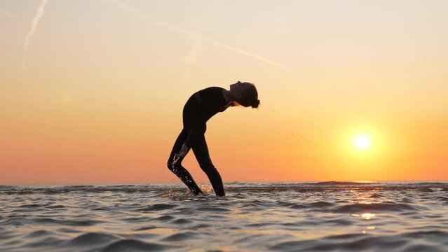 Young gymnast confidently executes back walkover with horizontal split, through handstand position. Her graceful silhouette stands out against sunset sky, as she showcases her skill