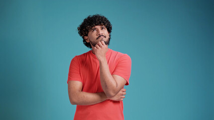 swarthy man in coral t-shirt on blue studio background thinking pondering looking for an idea.