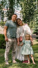 Naklejka na ściany i meble Portrait of a smiling young family mom dad and little daughter family on a walk in the park happy childhood