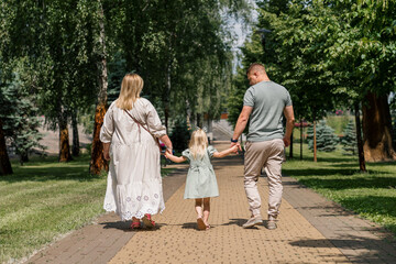 Little cute girl in green summer dress with parents in city park on a walk summer family lifestyle Childhood happy family rear view