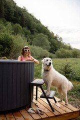 Woman bathing in outdoor hot tub while resting with her cute dog at house in mountains. Concept of...