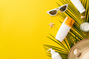 Relaxing under sun theme. Top view arrangement showcasing sunscreen bottles without labels, sunglasses, sunhat, seashells, starfish, palm leaf on bright yellow background with empty space for branding
