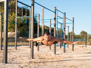 Young shirtless man performing a jump after doing a push-up at the outdoor calisthenics park - calisthenics concept.