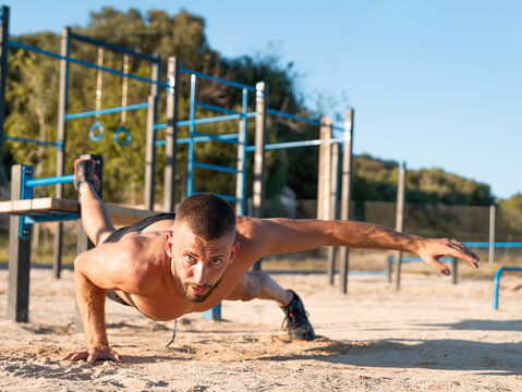 Young shirtless man performing one-arm push-ups at the outdoor calisthenics park - calisthenics concept.