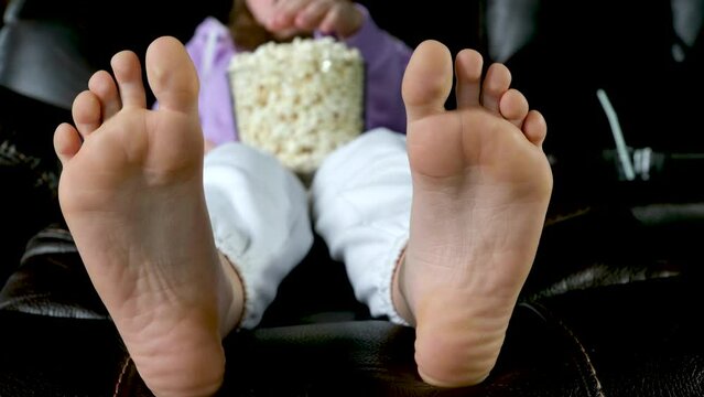 teenage sits on floor watches netflix on big screen of TV screensaver flashes on black background in red blue in hands young woman popcorn 