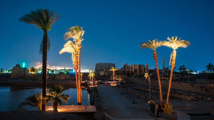 Sunset view at the illuminated temple of Karnak, Luxor, Egypt. Blue hour. View of the palm trees and the obelisk.