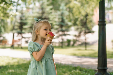 Fototapeta premium Little cute girl in green summer dress eating delicious ice cream Child with ice cream in city park summer family lifestyle Childhood