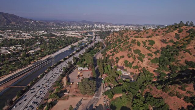 Drone aerial shot of Los Angeles traffic, cars, and vehicles moving on interstate multi-lane highway road system next to river and Griffith Park from above