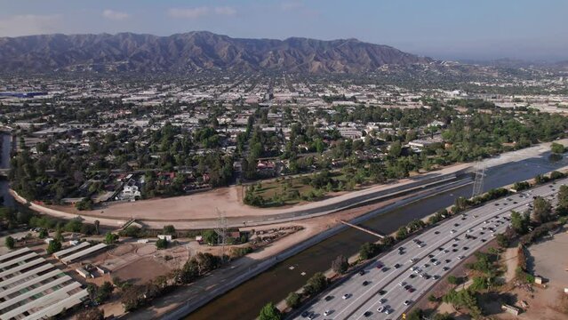 Drone aerial shot of Los Angeles traffic, cars, and vehicles moving on interstate multi-lane highway road system next to river and Griffith Park from above
