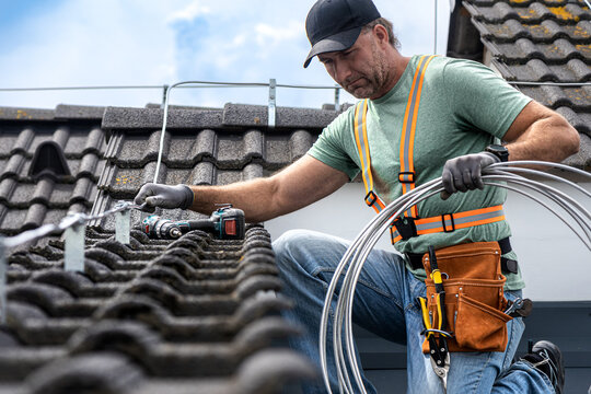 Work on the roof. An electrician installing a lightning rod conductor on a tiles roof.