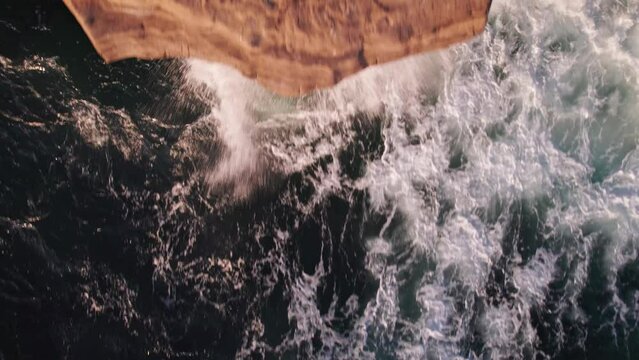 Aerial drone shot of big wave of water flowing across the Pacific Ocean surface towards a rocky shore and cliff around the sunset cliffs in southern California near San Diego