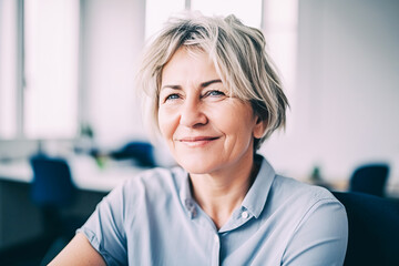 Beautiful middle aged woman with gray hair, office worker, looking at the camera and smiling while sitting