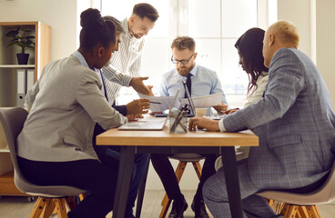 Group of business people working and communicating while sitting at office desk. Focused diverse colleagues in formal wear working on project, discussing financial documents, sharing ideas